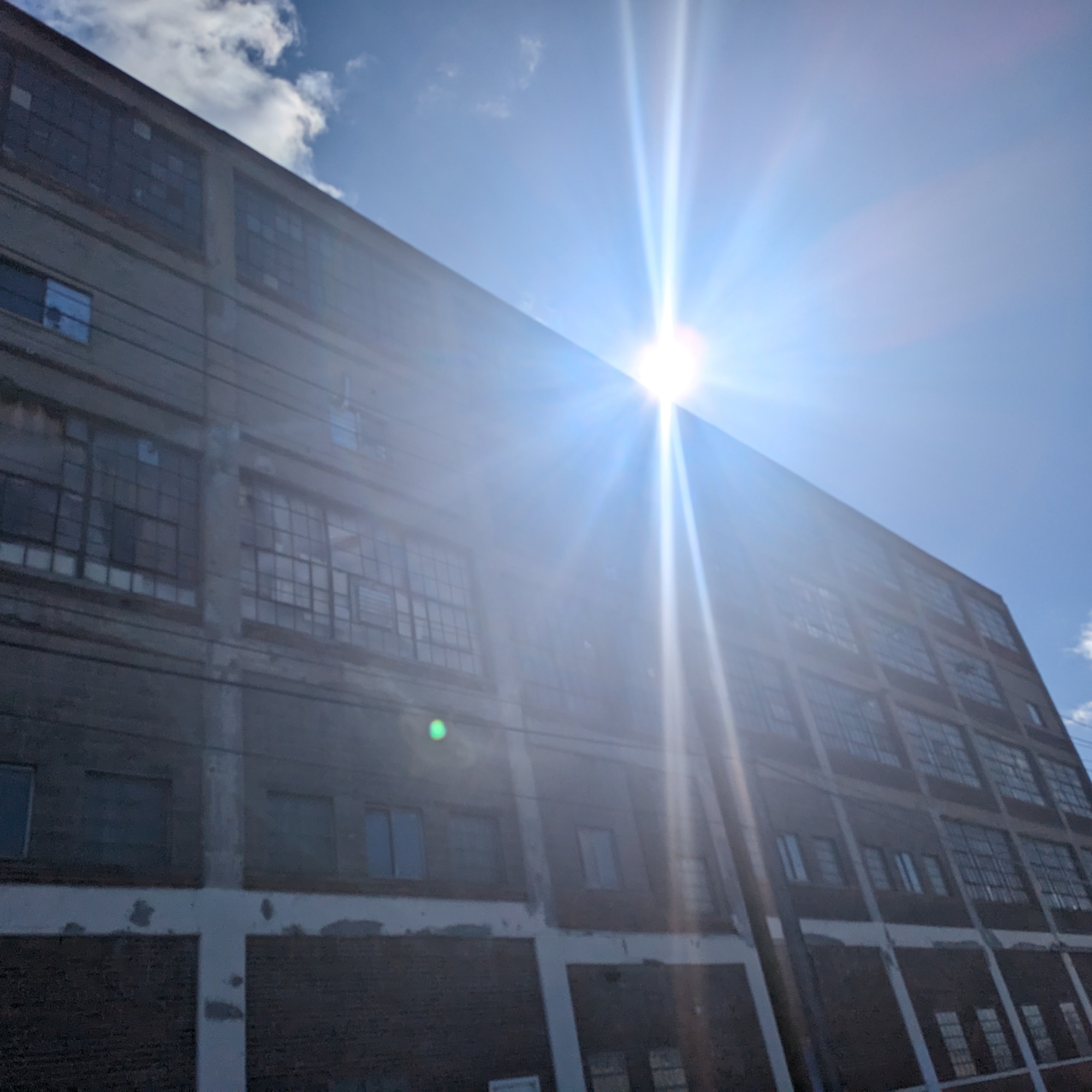 An image of the sun rising over a brick building in an urban landscape.