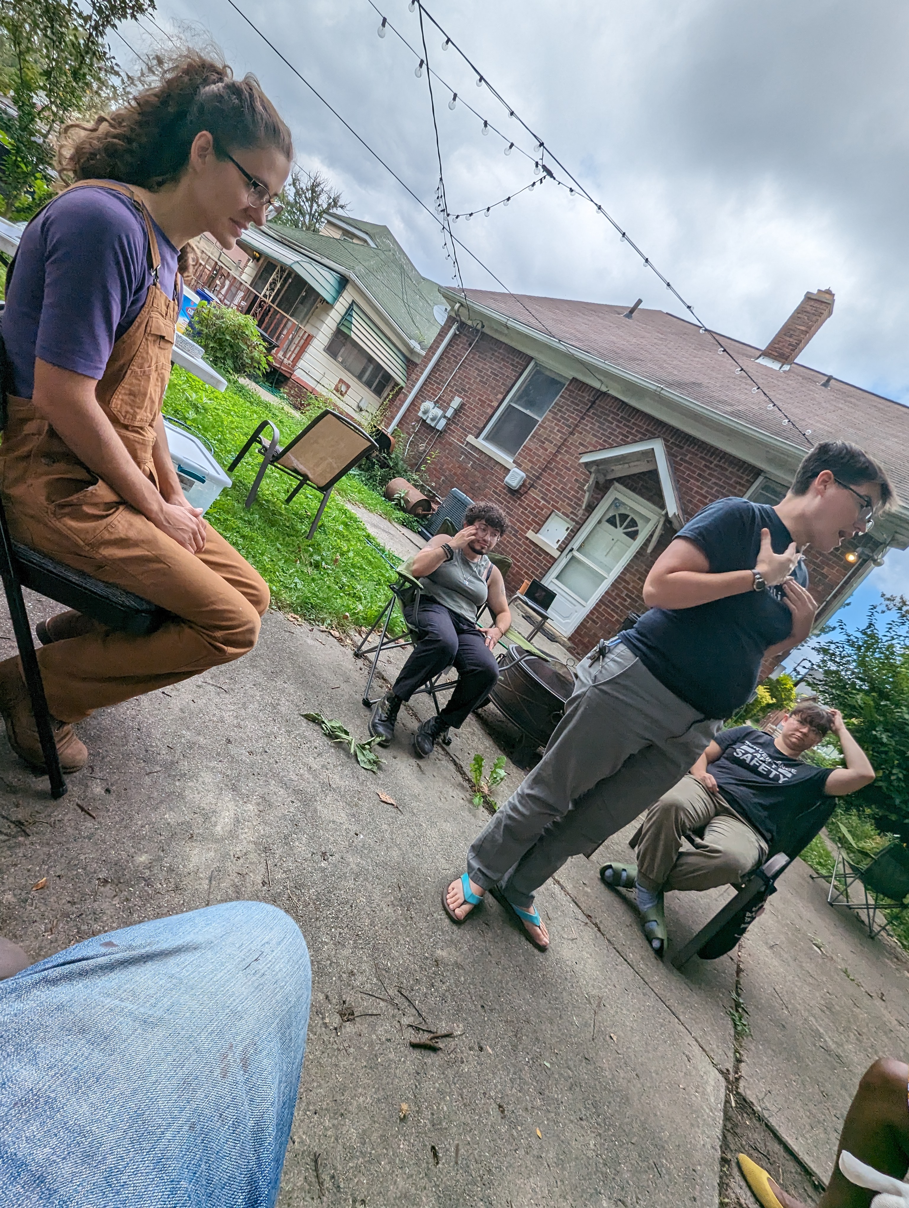 A photo of Detroit Peer Respite members sitting in a circle, taken from the perspective of someone sitting in the circle. Meg stands in the center, gesturing with their hands.