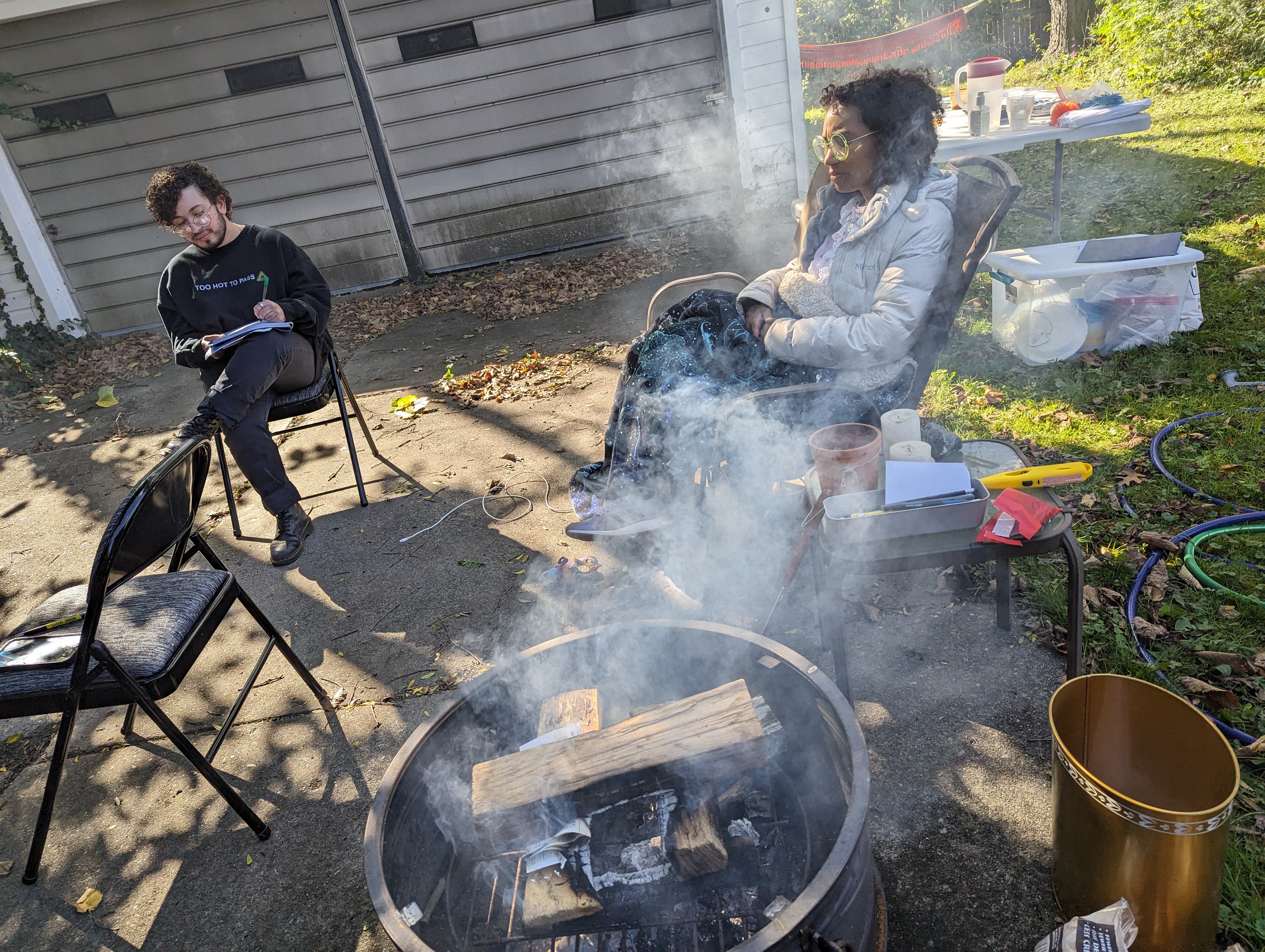 A photo of Karen and Grey, two members of Detroit Peer Respite. They are sitting on folding chairs huddled around a firepit.